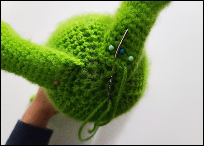Baby Grinch amigurumi seated pose showing detailed chubby cheeks and limbs