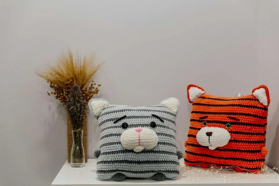 Handmade striped crochet cat pillow cushion styled on sofa with textured blanket