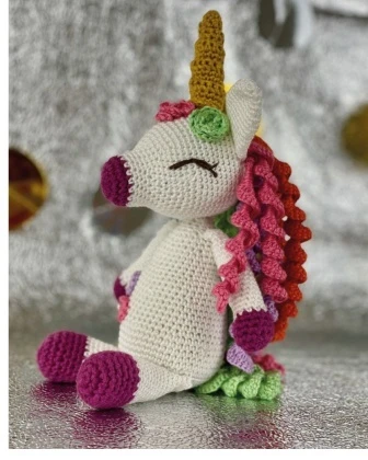 Side profile view of crochet sweet unicorn plush showing muzzle shape, sleepy eye and pink corkscrew mane